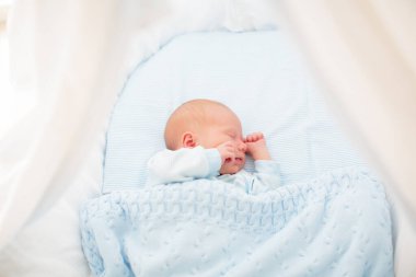 Yeni doğan bebek yatakta. Yeni doğan çocuk mavi örgü battaniye altında uyuyor. Çocuk uyku. Çocuklar için yatak takımları. Bebek yatakta uyuyor. Sağlıklı çocuk doğumdan kısa bir süre sonra. Kablo Tekstil Örme.