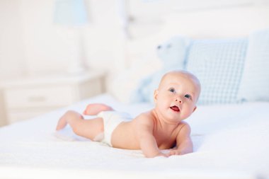 Erkek bebek bezi beyaz güneşli yatak odasında. Yeni doğan çocuk yatakta rahatlatıcı. Kreş çocuklar için. Tekstil ve çocuklar için yatak. Aile sabah evde. Oyuncak ayı ile mide süre içinde yeni doğmuş çocuk.