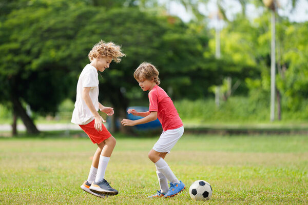 Ребенок играет в футбол. Дети играют в футбол на открытом поле. Мальчик пинает мяч в летнем парке. Здоровый образ жизни для маленьких детей. Школьный спортивный клуб. Юниорская лига.