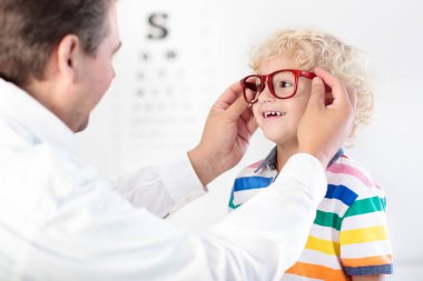 Çocuk göz testinde. Gözlükçüden gözlük seçen küçük bir çocuk. Okul çocukları için görüş ölçüsü. Çocuklar için göz giysisi. Doktor göz kontrolü yapıyor. Harf grafiğinde gözlüklü çocuk..