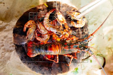 Sahildeki deniz ürünleri ızgarası. Istakoz, karides ve balık barbeküsü. Yaz tatilinde sağlıklı bir öğle yemeği. Kabuklu deniz hayvanı, mürekkep balığı ve karides ateşte kızartılmış. Tropik tatilde nefis bir akşam yemeği..