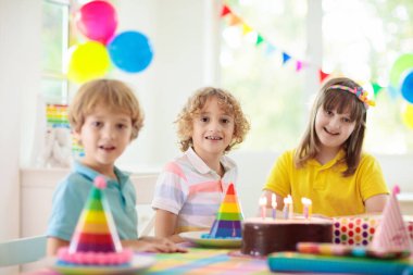Çocukların doğum günü partisi. Çocuk pastaya mum üflüyor ve hediyeleri açıyor. Pastel gökkuşağı temalı kutlama. Aile evde kutlama yapıyor. Çocuk hediyeleri açıyor, kek yiyor. Çocuklar için tatlılar.