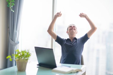 Şehir manzaralı büyük pencerede dizüstü bilgisayarda çalışan bir adam. Merkez ofis. Bilgisayarlı genç serbest çalışan bir erkek. Öğrenci çevrimiçi çalışıyor. Cep telefonu ve bilgisayarı olan adam. Evden çalış..