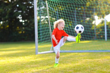 Çocuklar dışarıda futbol oynarlar. Çocuklar futbol maçında gol atıyor. Küçük çocuk topa vuruyor. Formalı ve kramponlu koşan çocuk. Okul futbol kulübü. Genç oyuncu için spor eğitimi.