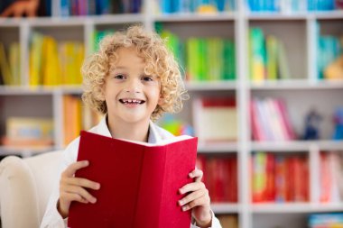 Çocuk kitabı okuyor. Çocuklar okur. Renkli bir kitaplıkta küçük bir çocuk okul için ödev yapıyor. Kitapları olan bir öğrenci. Erken eğitim ve gelişme. Çocuklar için ev kütüphanesi. Anaokulu öğrencisi..