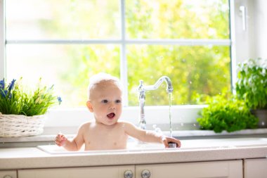 Bebek alarak banyo mutfak lavaboda. Köpük ve sabun köpüğü ile pencere güneşli banyoda ile oynayan çocuk. Küçük çocuk banyo. Su eğlenceli çocuklar için. Hijyen ve Cilt Bakımı Çocuk için. Banyo odası iç