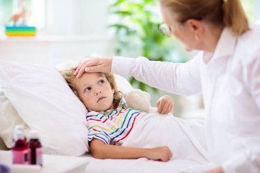 Hasta küçük çocuk ilaçla. Anne yatakta hasta çocuk ateşini kontrol ediyor. Astım tedavisi için astım spreyi olan hasta bir çocuk. Grip mevsimi. Ebeveyn yatak odasında ya da genç hastalar için hastane odasında.