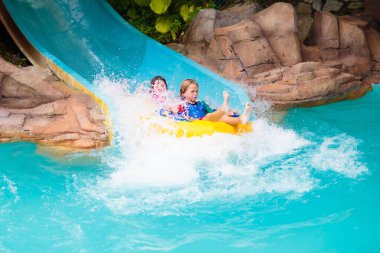 Çocuklar yüzme havuzunda su kaydırağında. Aqua tema parkında bir aile. Çocuklar su sıçratma parkında eğlenirler. Çocukla yaz tatili. Havuza kayan şişme tüplü çocuk..