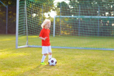 Çocuklar dışarıda futbol oynarlar. Çocuklar futbol maçında gol atıyor. Küçük çocuk topa vuruyor. Formalı ve kramponlu koşan çocuk. Okul futbol kulübü. Genç oyuncu için spor eğitimi.