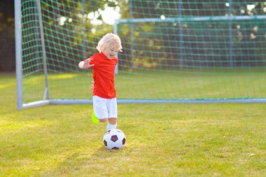 Çocuklar dışarıda futbol oynarlar. Çocuklar futbol maçında gol atıyor. Küçük çocuk topa vuruyor. Formalı ve kramponlu koşan çocuk. Okul futbol kulübü. Genç oyuncu için spor eğitimi.