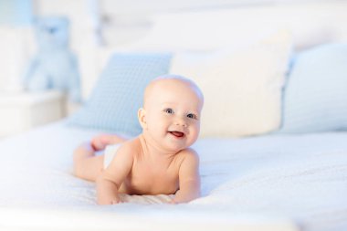 Erkek bebek bezi beyaz güneşli yatak odasında. Yeni doğan çocuk yatakta rahatlatıcı. Kreş çocuklar için. Tekstil ve çocuklar için yatak. Aile sabah evde. Oyuncak ayı ile mide süre içinde yeni doğmuş çocuk.