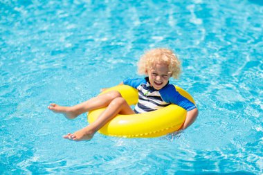 Yüzme havuzunda şişme yüzük takan çocuk. Sarışın kıvırcık çocuk yüzmeyi ve açık havuza dalmayı öğreniyor. Çocuklarla yüzmek. Çocuklar için sağlıklı yaz sporları aktivitesi. Güneş koruması. Su eğlencesi