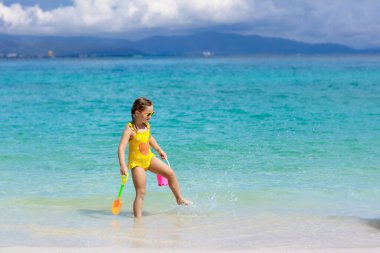 Tropik plajda oynayan bir çocuk. Deniz kıyısındaki küçük kız. Aile yaz tatili. Çocuklar su ve kum oyuncaklarıyla oynuyor. Okyanus ve ada eğlencesi. Küçük çocuklarla seyahat et. Asya tatili.