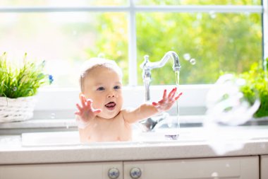 Bebek alarak banyo mutfak lavaboda. Köpük ve sabun köpüğü ile pencere güneşli banyoda ile oynayan çocuk. Küçük çocuk banyo. Su eğlenceli çocuklar için. Hijyen ve Cilt Bakımı Çocuk için. Banyo odası iç