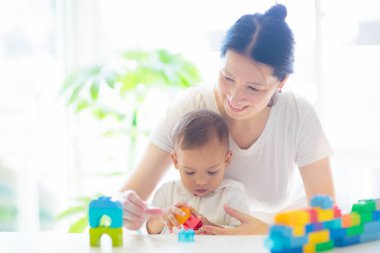 Asyalı anne ve bebek beyaz güneşli yatak odasında renkli blok oyuncaklarıyla oynuyor. Anne ve bebek eğitici oyuncaklarla. Çocuk yapım kulesi. Zeki çocuklar için erken gelişim. Çocuk odası eğlencesi.