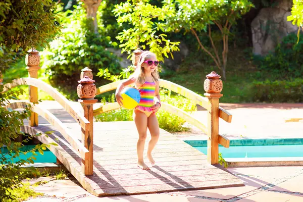 Havuzda şişme oyuncak topu olan bir çocuk. Çocuklar yüzer. Genç çocuklar için renkli gökkuşağı yüzüyor. Küçük kız yaz tatilinde tropikal tatil köyünde eğleniyor. Kumsal ve su eğlencesi. 