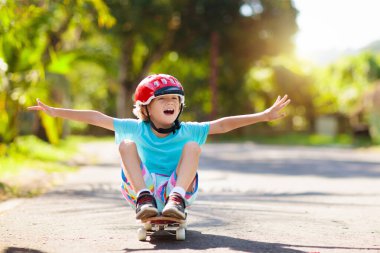 Kaykaylı çocuk. Çocuk kaykay tahtası. Yazın okul çocukları için sağlıklı spor ve açık hava aktiviteleri. Spor eğlencesi. Güvenli egzersiz için kask. Güneşli parkta buz patencisi. Çocuk eğitimi.