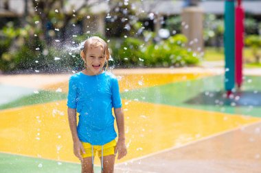 Su parkında bahşiş kovasının altında oynayan bir çocuk. Çocuklar çöp kovasıyla oynarlar. Sıcak yaz gününde eğlence merkezinde aile eğlencesi. Çocuklar için güneş koruması. Çocuk için su kaydırakları.