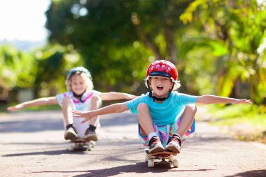 Kaykaylı çocuk. Çocuk kaykay tahtası. Yazın okul çocukları için sağlıklı spor ve açık hava aktiviteleri. Spor eğlencesi. Güvenli egzersiz için kask. Güneşli parkta buz patencisi. Çocuk eğitimi.