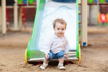 Güneşli bir yaz gününde parkta oynayan bir çocuk. Çocuklar sallanıyor ve kayıyor. Okul ya da anaokulu bahçesi ve oyun alanı. Yazın açık hava aktivitesi. Oynayan çocuk.