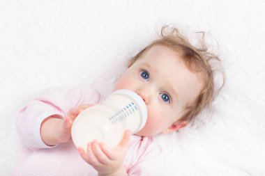 Beyaz güneşli yatak odasında sevimli bir bebek. Yeni doğmuş çocuk yatakta dinleniyor. Küçük çocuklar için çocuk odası. Çocuklar için tekstil ve yatak. Aile sabahı evde. Oyuncak ayıyla karnını doyururken doğan yeni çocuk..