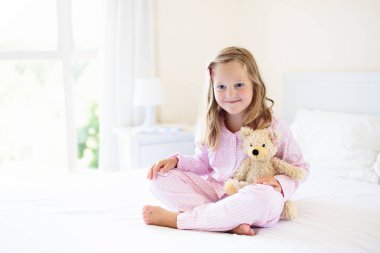 Anne yatakta oynayan çocuklar. Çocuklar güneşli beyaz yatak odasında uyan. Küçük kız pembe pijama. Pijama ve yatak çocuk ve bebek için. Yürümeye başlayan çocuk için çocuk odası iç. Aile sabah.