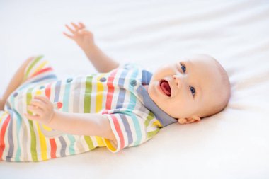 Beyaz güneşli yatak odasında sevimli bir bebek. Yeni doğmuş çocuk yatakta dinleniyor. Küçük çocuklar için çocuk odası. Çocuklar için tekstil ve yatak. Aile sabahı evde. Oyuncak ayıyla karnını doyururken doğan yeni çocuk..