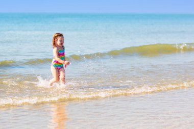 Tropik plajda oynayan çocuklar. Su sıçratma eğlencesi. Deniz dalgalarında süzülen küçük çocuk. Çocuklar yaz tatilinde yüzer ve oynarlar. Kum ve su oyuncağı, küçük çocuklar için güneş koruması.. 