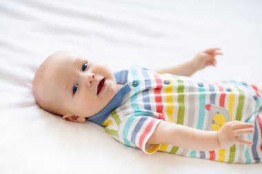 Beyaz güneşli yatak odasında sevimli bir bebek. Yeni doğmuş çocuk yatakta dinleniyor. Küçük çocuklar için çocuk odası. Çocuklar için tekstil ve yatak. Aile sabahı evde. Oyuncak ayıyla karnını doyururken doğan yeni çocuk..