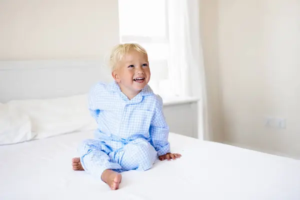 stock image Kids playing in parents bed. Children wake up in sunny white bedroom. Little boy in blue pajamas. Sleepwear and bedding for child and baby. Nursery interior for toddler kid. Family morning.