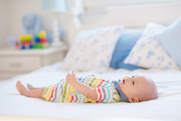 Adorable baby in white sunny bedroom. Newborn child relaxing in bed. Nursery for young children. Textile and bedding for kids. Family morning at home. New born kid during tummy time with toy bear.