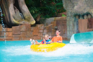 Çocuklar yüzme havuzunda su kaydırağında. Aqua tema parkında bir aile. Çocuklar su sıçratma parkında eğlenirler. Çocukla yaz tatili. Havuza kayan şişme tüplü çocuk..