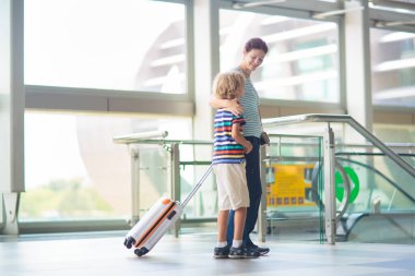Ailesi havaalanında. Anne ve çocuk hava yoluyla seyahat ediyorlar. Uç ve çocuklarla seyahat et. Küçük çocuk ve annesi havaalanı terminali koridorundaki uçağa doğru yürüyorlar. Tatil ya da iş gezisi. Çocuklarla tatil.