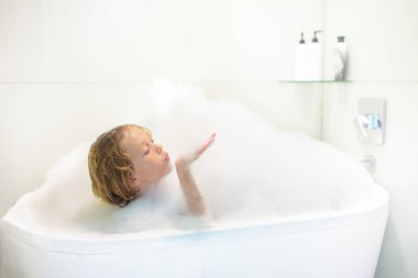 Çocuk banyoda sabun köpüğüyle oynuyor. Küçük çocuk banyo yapıyor ve saçlarını çocuk şampuanıyla yıkıyor. Çocuklar için hijyen ve uyku zamanı rutini. Deri ve vücut bakımı.