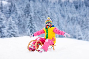 Küçük kız kızakla gezintiye çıkıyor. Çocuk kayağı. Kızak süren küçük bir çocuk. Çocuklar karda dışarıda oynarlar. Çocuklar kışın Alp dağlarında kızak kullanırdı. Aile Noel tatili için açık hava eğlencesi.