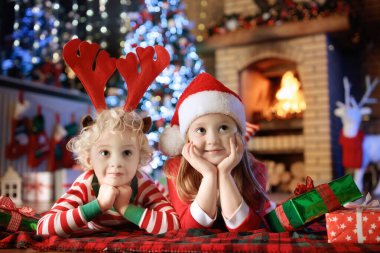 Noel arifesinde Noel ağacı ve şömine başında çocuklar. Noel 'i evde kutlayan çocuklu bir aile. Erkek ve kız aynı pijamaları giyip Noel ağacını süslüyor ve hediyeleri açıyor. Çocuklar için tatil hediyeleri.