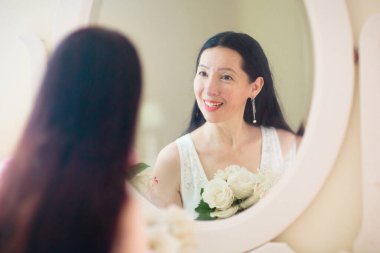 Genç Asyalı kadın aynaya bakıyor. Cilt bakımı rutini. Randevu gecesi ya da hafta sonu sabahında krem süren gecelikli güzel bir kadın. Deri temizleme ve tedavi. Mücevher ve inciler.. 