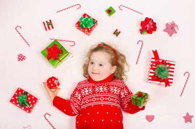 Çocuk Noel hediyeleri açma. Örme kış kazak mevcut kutusuyla, küçük kız. Çocuklara hediyeler açın. Yürümeye başlayan çocuk dekore edilmiş Xmas ağacı altındaki katta. Hediye kutusu ve şeker ile çocuk oyun.