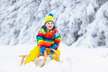 Küçük çocuk kızakla gezintiye çıkıyor. Çocuk kayağı. Kızak süren küçük bir çocuk. Çocuklar karda dışarıda oynarlar. Çocuklar kışın Alp dağlarında kızak kullanırdı. Aile Noel tatili için açık hava eğlencesi.