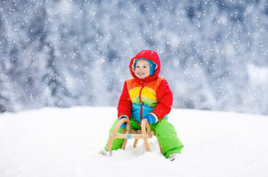 Küçük çocuk kızakla gezintiye çıkıyor. Çocuk kayağı. Kızak süren küçük bir çocuk. Çocuklar karda dışarıda oynarlar. Çocuklar kışın Alp dağlarında kızak kullanırdı. Aile Noel tatili için açık hava eğlencesi.