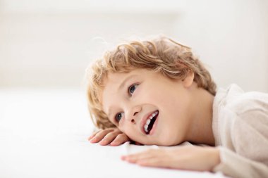 Pencereden dışarı bakıp gülümseyen bir çocuk. Beyaz yatakta küçük bir çocuk. Mutlu çocuk gülüyor ve oynuyor.