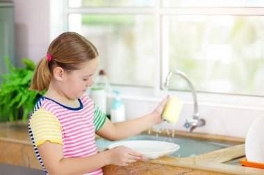 Çocuk bulaşık yıkıyor. Ev işleri. Öğle yemeğinden sonra beyaz mutfakta tabakları temizleyen bir çocuk..