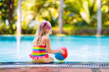 Havuzda şişme oyuncak topu olan bir çocuk. Çocuklar yüzer. Genç çocuklar için renkli gökkuşağı yüzüyor. Küçük kız yaz tatilinde tropikal tatil köyünde eğleniyor. Kumsal ve su eğlencesi. 