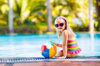 Havuzda şişme oyuncak topu olan bir çocuk. Çocuklar yüzer. Genç çocuklar için renkli gökkuşağı yüzüyor. Küçük kız yaz tatilinde tropikal tatil köyünde eğleniyor. Kumsal ve su eğlencesi. 