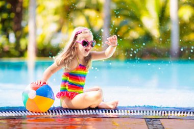 Havuzda şişme oyuncak topu olan bir çocuk. Çocuklar yüzer. Genç çocuklar için renkli gökkuşağı yüzüyor. Küçük kız yaz tatilinde tropikal tatil köyünde eğleniyor. Kumsal ve su eğlencesi. 