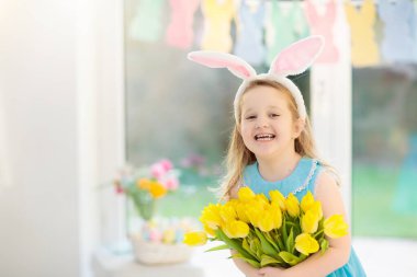 Lale çiçek buketi tutan tavşan kulakları mutlu küçük kız. Çocukları Paskalya kutlamak. Çocuk Paskalya yumurtası avına eğleniyor. Ev Dekorasyon, pastel bunny afiş, renkli yumurta ve bahar çiçekleri. 