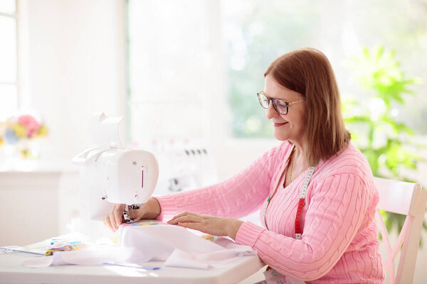 Женщина шьет за белым столом. Семинар по дизайну одежды. Творческая хитрость и безумие. Одежда ручной работы. Портной или швея рабочее место с оверлок машины. Женское платье. Швейное оборудование и инструменты