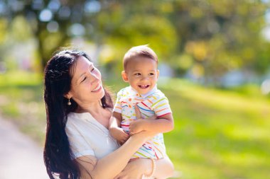 Sunny Park 'ta anne ve oğlu. Dışarıda oynayan Asyalı bir aile. Anne kucağında küçük bir çocuk var. Genç bir kadın ve sevimli bir çocuk oynuyorlar ve gülüyorlar. Mutluluk ve sevgi. Anneler günün kutlu olsun..