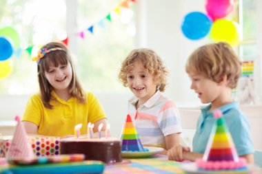 Çocukların doğum günü partisi. Çocuk pastaya mum üflüyor ve hediyeleri açıyor. Pastel gökkuşağı temalı kutlama. Aile evde kutlama yapıyor. Çocuk hediyeleri açıyor, kek yiyor. Çocuklar için tatlılar.