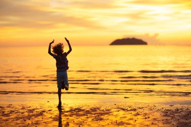 Okyanus sahilinde oynayan bir çocuk. Gün batımında dalgalara atlayan bir çocuk. Aile için deniz tatili. Yaz tatili boyunca egzotik adada koşan küçük çocuk.. 